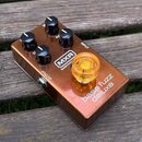 Koparově hnědý kytarový efekt s nápisy MXR, BASSINNOVATION a bass fuzz deluxe. Zařízení má čtyři černé otočné knoflíky s bílými značkami a jeden velk…