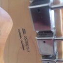 Detail zadní strany hlavy kytary z přírodního dřeva s chromovanými ladičkami. Na dřevě je černý nápis SERIAL NUMBER US23027215 CORONA, CALIFORNIA. Po…