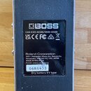 Zadní strana efektového pedálu značky BOSS v šedé barvě. Na černé nálepce jsou uvedeny nápisy CAN ICES-003(B)/NMB-003(B), různé certifikační loga, te…