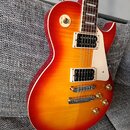 Elektrická kytara s tvarem singlecut a povrchovou úpravou v červeno-žlutém sunburstu. Nástroj má dva humbuckery s bílými rámečky, čtyři zlaté ovládac…