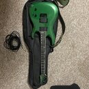 Zelená elektrická kytara s dvěma humbuckery, položená na černém softcasu. Na hlavě kytary je viditelné logo "Jay Tour". K nástroji patří zelený popru…