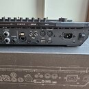Zadní strana černého elektronického hudebního zařízení s řadou konektorů. Jsou zde nápisy OUTPUTS, NEXUS, S/PDIF a MIDI, dále označení L/MONO, RIGHT,…