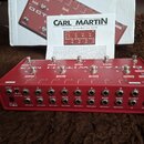 Červený kovový pedalboard s nápisem OCTA-SWITCH MK3 a logem CARL MARTIN. Zařízení má osm přepínačů, několik malých bílých přepínačů a řadu konektorů…