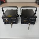 Dvě identické černé elektronické jednotky s úchytkami. Na přední straně každé jednotky je digitální displej, nápisy ILDA OUTPUT, ILDA INPUT, DMX IN,…