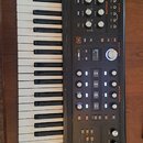 Černý syntetizátor s klaviaturaí. Na horním panelu je oranžové logo ASM Electric Music Company a nápis HYDRASYNTH. Přístroj obsahuje numeroustovací k…