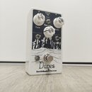 Bílý kytarový efekt s černým grafickým potiskem krajiny. Na horní straně jsou tři bílé otočné knoflíky s popisky Tone, Volume a Gain, dva přepínače o…