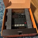 Černý digitální syntetizátor Digitone umístěný v originálním hnědém kartónovém boxu s pěnovými vložkami. Na přístroji je vidět nápis Digitone a logo…