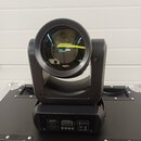 Černý LED moving head reflektor umístěný na transportním kufru. Na zadní straně přístroje je digitální displej a ovládací tlačítka, nad nimi je nápis…