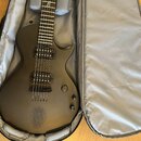 Černá elektrická kytara s matným povrchem v převozném pouzdře. Na hlavě je viditelné logo značky ESP. Tělo kytary má dva humbuckery, jeden ovládací k…