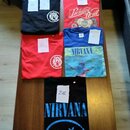 Pět triček rozložených na hnědém stole. Jsou zde dvě černá, dvě červená a jedno modré tričko s potisky kapel Nirvana a Parkway Drive. Na každém kuse…