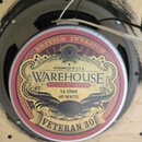 Kytarový reproduktor s kulatým štítkem v červeně, žluté a černé barvě. Na štítku jsou nápisy BRITISH INVASION, ASSEMBLED IN U.S.A., WAREHOUSE GUITAR…