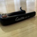 Černý kytarový kapodastr s kovovou pružinou. Na boku je bílým nápisem uveden název Guitto a model GGC-03. Povrch je hladký, v místě uložení pružiny j…