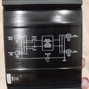 Černý kovový přístroj s broušeným povrchem. Na horní straně je bílý schéma s nápisy: ISOLATED SPLIT OUTPUT, COMBINED MIC INPUT, PHASE (NORMAL, INVERT…