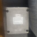 Fotografie zachycuje spodní stranu stříbrného, hranatého elektronického zařízení s čtyřmi gumovými nožičkami. Na spodní straně je viditelná nálepka s…