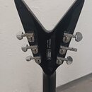Zadní strana černé kytary s hlavou ve tvaru V a chromovanými ladičkami. Na zadní straně hlavy je bílý nápis H2050186, Made in India a loga CE a RoHS…
