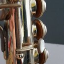 Detailní záběr na část hřidlu klarnetu s kovovým povrchem. Jsou vidět klapky s hnědými polštářkami a jedna bílá perleťová klapka. Povrch nástroje vyk…