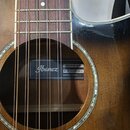 Detail akustické kytary s hnědým povrchem a hředníkem z tmavého dřeva. Uvnitř otvoru kytary je nalepený štítek s nápisy Ibanez, MODEL NO. ASG10121-DV…