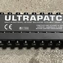 Černý rackový patchbay s nápisem ULTRAPATCH a podtitulem MULTI-FUNCTIONAL 48-POINT BALANCED PATCHBAY MODEL PX1000. Na předním panelu je logo BEHRINGE…