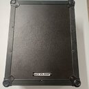 Černý transportní kufr s kovovými hranami a rohovými zpevněními. Na spodní hraně je umístěn bílo-černý štítek s nápisem RELOOP. Povrch kufru je v dob…