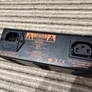 Černý napájecí adaptér s dvěma konektory. Na spodní straně je bílá nálepka s texty CAUTION, WARNING, AVIS a ATTENTION, specifikací 110-120V T1A L250V…