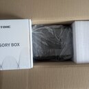 V hnědé kartonové krabici se nachází bílé papírové balení s nápisy HOTONE a ACCESSORY BOX. Vedle něj je tmavý, pravděpodobně plastový předmět zabalen…