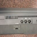 Zadní strana černého elektronického hudebního zařízení z plastu. Jsou zde viditelné nápisy AUX OUT, L/R, AC INLET, MIC INPUT, THRU, FOOT SWITCH a FOO…