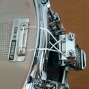 Detailní záběr na snare drum s chromovaným obručem a bílým blátcem. Na kovovém držáku je vyražen nápis SONOR SW 1418 S. Nástroj vykazuje známky běžné…