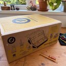 Kartonová krabice s nápisem MOOG SOUND STUDIO a MOTHER-32 & DFAM. Na povrchu je schéma nástrojů, logo Moog a seznam obsahu v sekci WHAT'S IN THE BOX.…