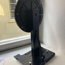 Černý kovový stojan s kulatým horním prvkem, který připomíná buben nebo držák. Celý předmět je lakovaný na černo a nemá žádné viditelné značky, loga…