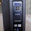 Černý reproduktor s texturovaným povrchem. Na zadním panelu je nápis SIENA a logo Turbosound s doplňkem DESIGNED AND ENGINEERED IN ENGLAND. Horní čás…