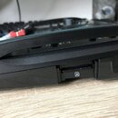 Detailní záběr na zadní část černého elektronického zařízení z plastu. Jsou vidět dva konektory: slot pro paměťovou kartu s ikonou trojúhelníku a USB…