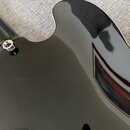 Detailní záběr na černý, lesklý povrch těla elektrické kytary. Na fotce je vidět část hředu a jeden kovový šroub s podložkou. Povrch je hladký a vyso…