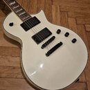 Bílá elektrická kytara s dvěma černými humbuckery a čtyřmi ovládacími knoflíky. Tělo má zaoblený tvar s bílým lemováním po okrajích. Na povrchu jsou…