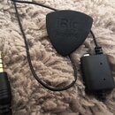 Černý rozhraní iRig Acoustic v podobě trsátka s připojeným kabelem a konektorem. Na trsátku je vyražen nápis iRig Acoustic. Povrch plastu je matný a…