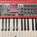 Červený digitální klavír s bílými a černými klávesami. Na pravé straně je bílý nápis nord electro 6 HP a pod ním menší text HAMMER ACTION PORTABLES.…