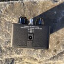 Zadní strana černého kytarového efektu s texturovaným povrchem. Na zadní straně je bílý nápis: „Designed in USA i Made in China 26580 Agoura Rd., Cal…