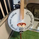 Bílá kruhová membrána kontrabasu s dřevěným hřádem. Na povrchu je černý nápis „Country music session“ vlevo a „Kontrabanyo Basofon“ vpravo. Uprostřed…