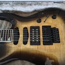 Elektrická kytara s tělem v žlutém gradientu (burst) a černými okraji, položená v polstrovaném kufru. Nástroj má tři humbuckery, černý most s páčkou…