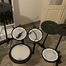 Elektronická bicí souprava s černým rámem a bílými padovými plochami. Na padách jsou viditelné nápisy Roland a V-Drums. Součástí je ovládací modul s…