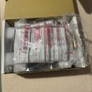 V kartónové krabici je v ochranné fólii zabalený produkt s přiloženou dokumentací. Na viditelných papírech jsou texty v několika jazycích, včetně náp…