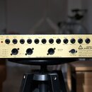 Zadní strana rackového audio zařízení s černým šasi a zlatým zadním panelem. Jsou zde viditelné konektory pro Main Outputs, Aux Inputs, Post Stereo E…