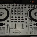 Stříbrný DJ 컨트롤러 s dvěma velkými černými jogovými koly. V horní části je nápis TRAKTOR KONTROL S4 a v dolní části logo TRAKTOR. Přístroj obsahuje poč…