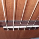 Detailní záběr na kobylku akustické kytary s bílým kostěným nebo plastovým sedlem. Kobylka je vyrobena z tmavého dřeva a jsou v ní upevněny šesty str…
