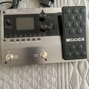 Stříbrný kytarový procesor s černým expresním pedálem, na kterém je bílý nápis MOER. Na horní části přístroje je text GE150 Amp modelling & Multi Eff…
