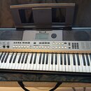 Stříbrný digitální klavír v černé přepravní tašce s přiklopnou hudební notovou deskou. Na přístroji je viditelné logo YAMAHA a označení modelu PSR-E4…