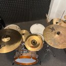 Sada bubnů s činely v dřevěném provedení. Na činelech jsou viditelné loga Zildjian, u jednoho z nich nápisy CUSTOM a K. Na bubnových blanách je čitel…
