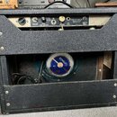 Zadní strana kytarového komba v černém texturovaném potahu. Na horním ovládacím panelu jsou nápisy: „0.7 AMP 117 VOLTS 60 CYCLE“, „ON“, „FENDER ELECT…