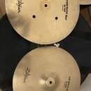 Dva mosazné činely typu hi-hat položené na černém obalu. Horní činel má nápisy Zildjian a BOTTOM QUICK BEAT HI HAT 14"35cm. Dolní činel nese nápisy Z…