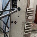 Zadní strana kovového elektronického zařízení stříbrné barvy s hliníkovým chladičem na pravé straně. V horní části jsou umístěny konektory, včetně je…