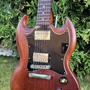 Elektrická kytara s hnědým dřevěným tělem a tmavým hnedým plechtrátem. Nástroj má dva humbuckery s kovovými kryty, čtyři otočné knoflíky a přepínač s…
